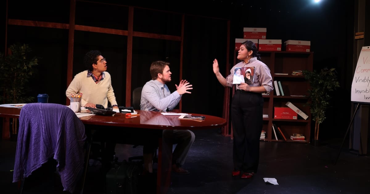 Three actors perform a scene in a conference room