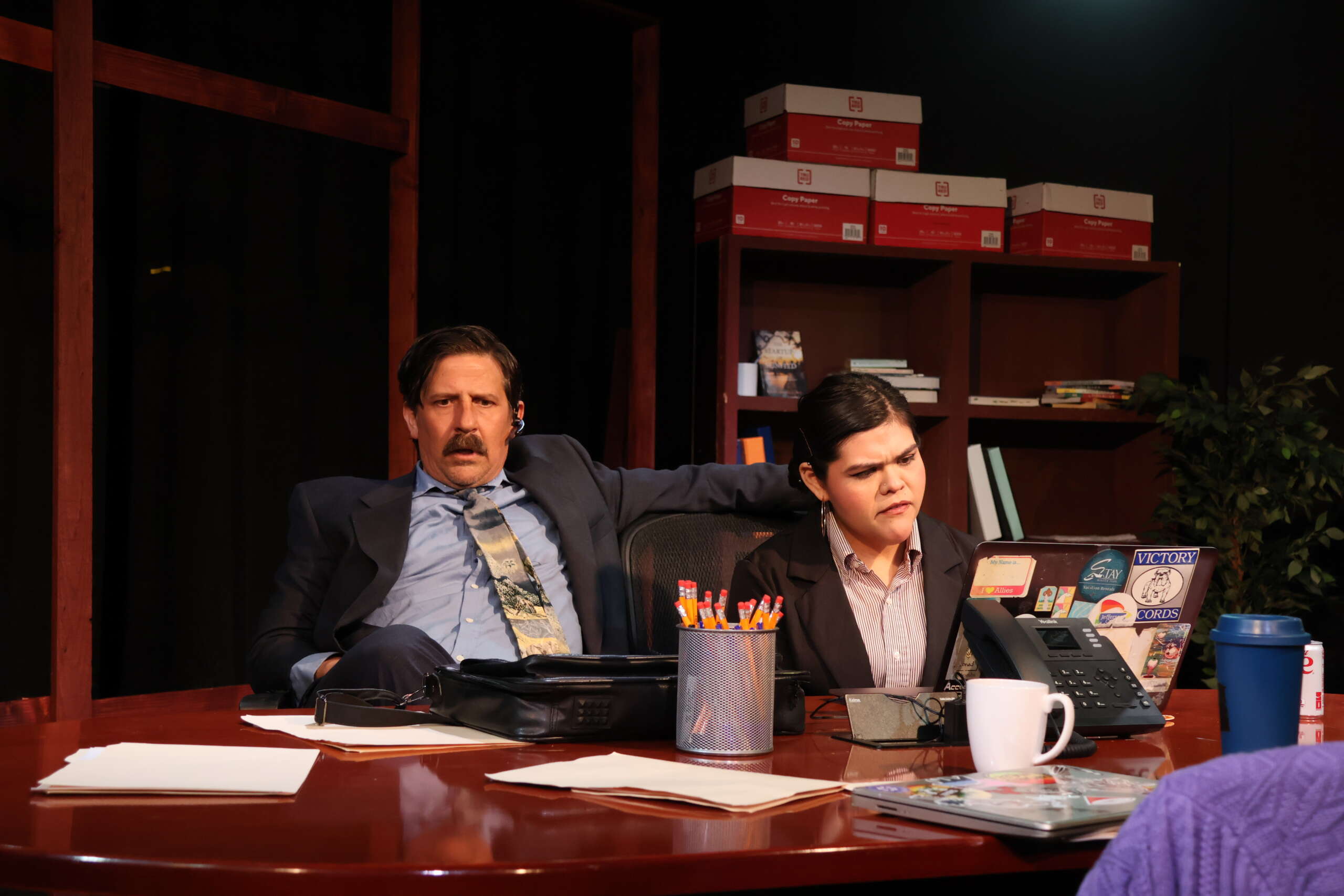 A man and a woman sit in a conference room in a play
