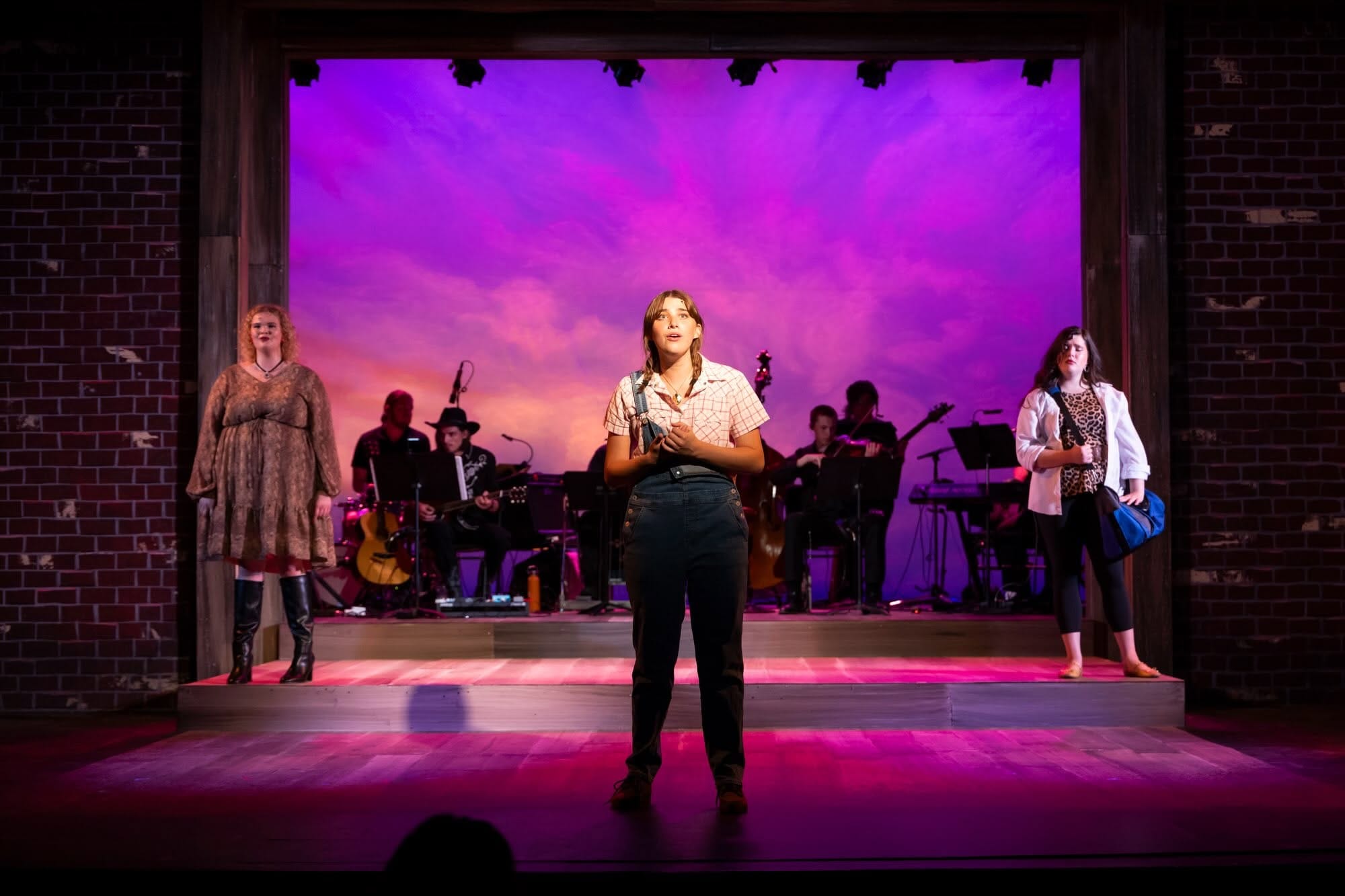 Three woman sing onstage with a band behind them