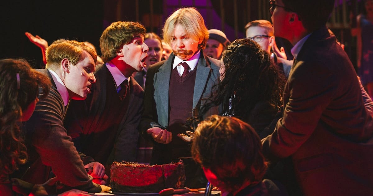 People surround a boy eating a chocolate cake