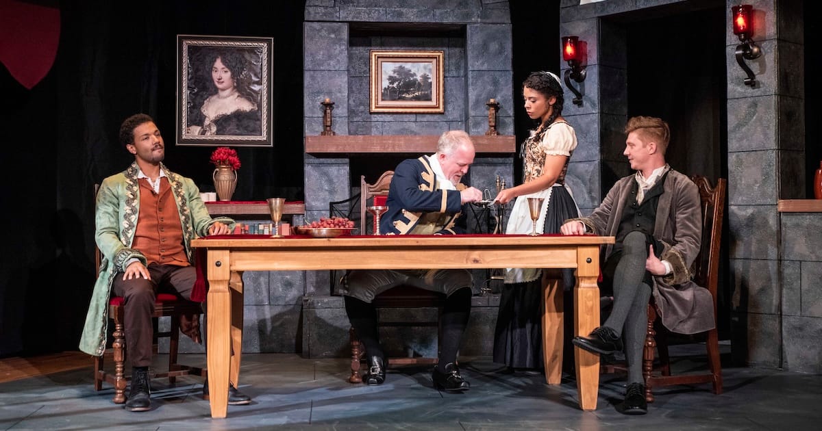 Three men sit at a table while a woman stands