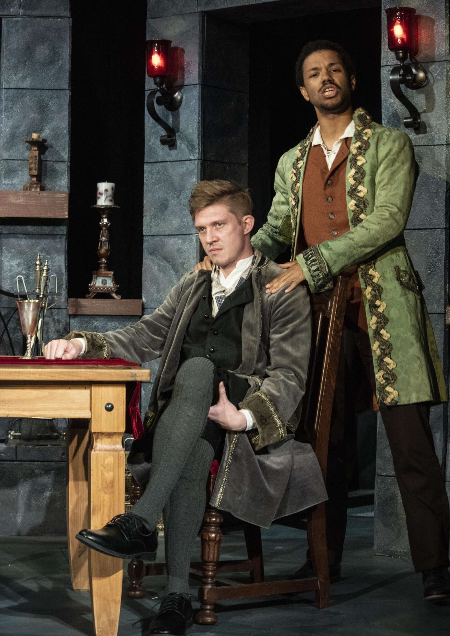 A man grasp an angry-looking man who is sitting down by the shoulder