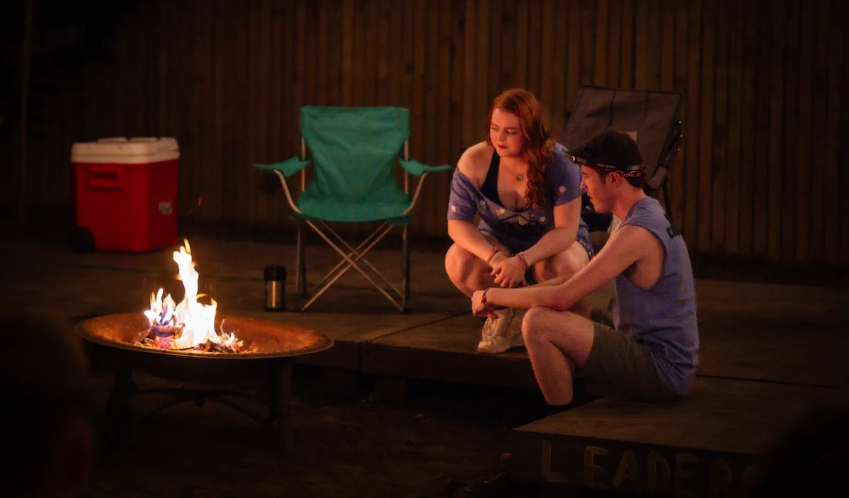 Two people sit around a campfire in The Grown-Ups