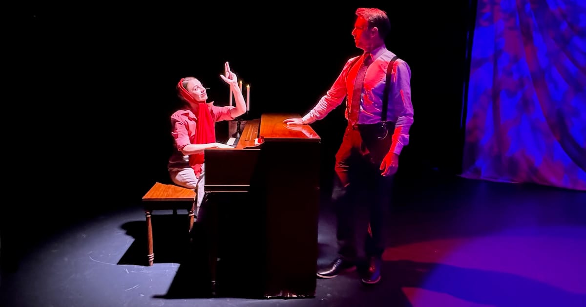 A woman does a finger guns at a piano while a man stands nearby in a scene from Murder for Two