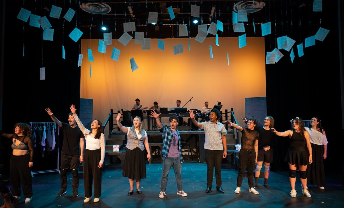 A group of actors gestures upwards onstage