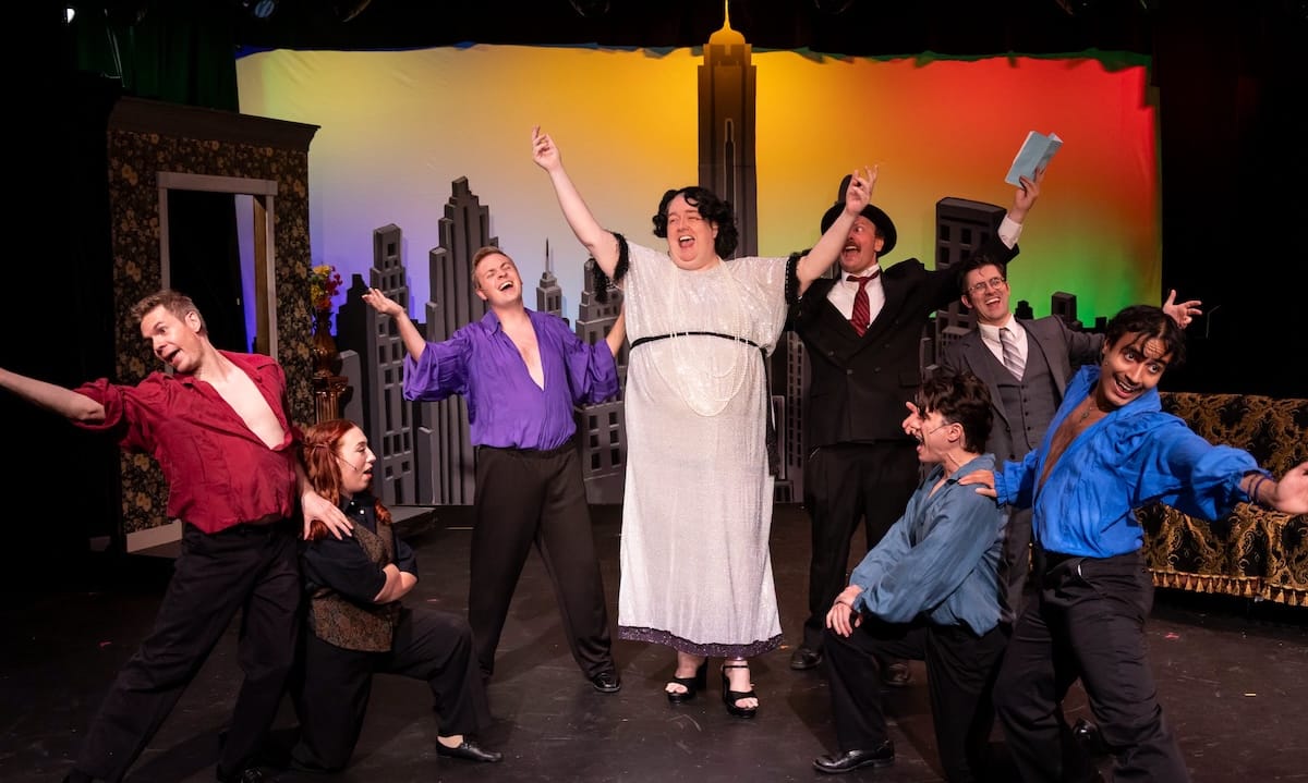 A group of people sing onstage surronded by a rainbow in The Producers