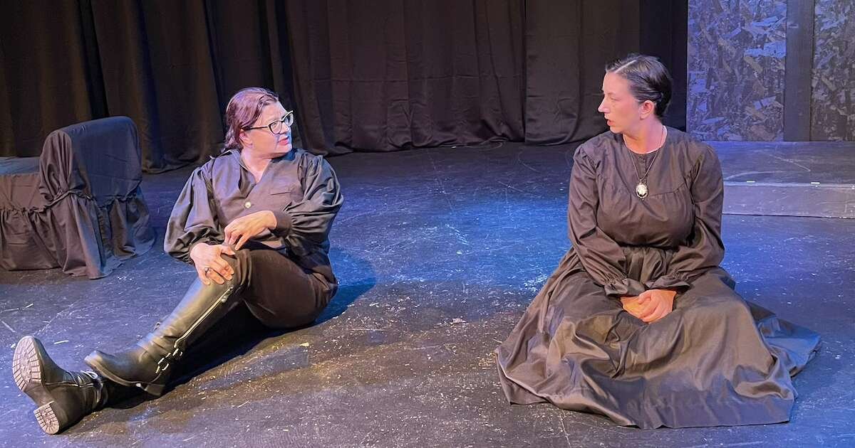 Two women sit on the ground and talk during a scene from 